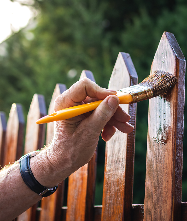 Painting protective varnish on wooden picket fence at backyard